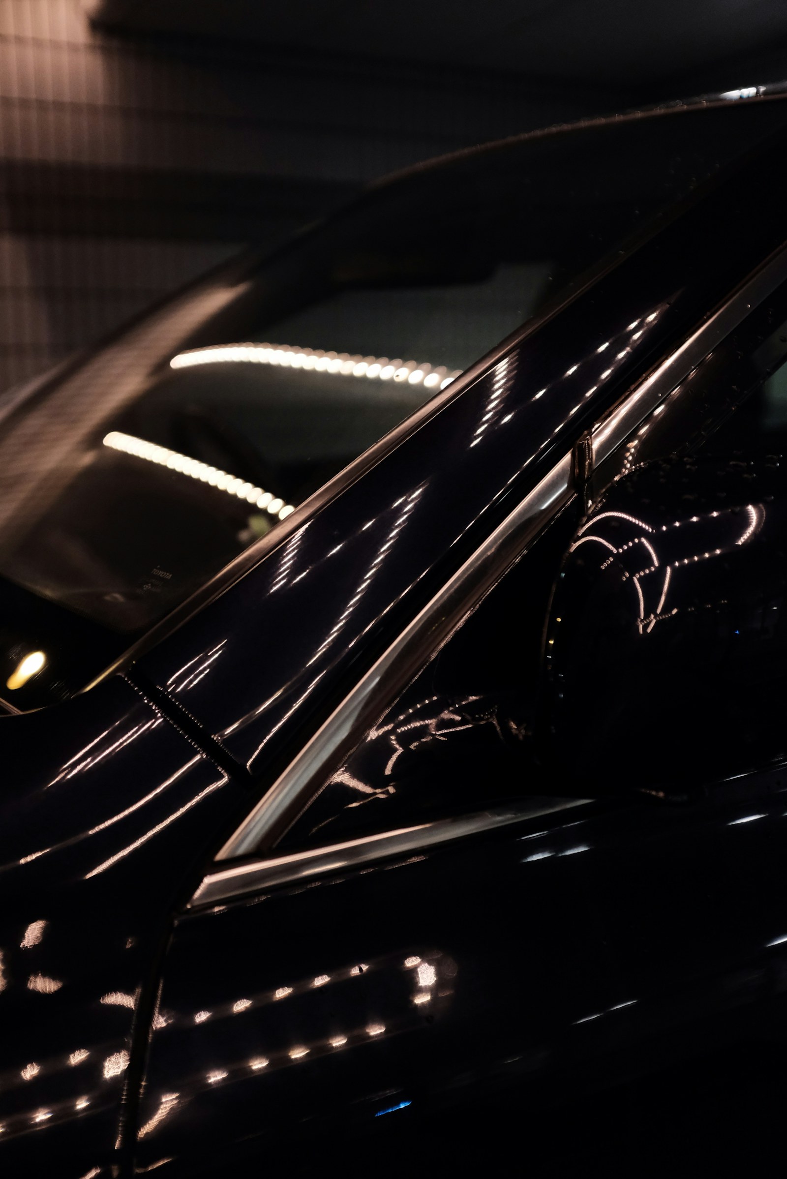 Light strips reflected in the deep black tint of a car’s front quarter glass